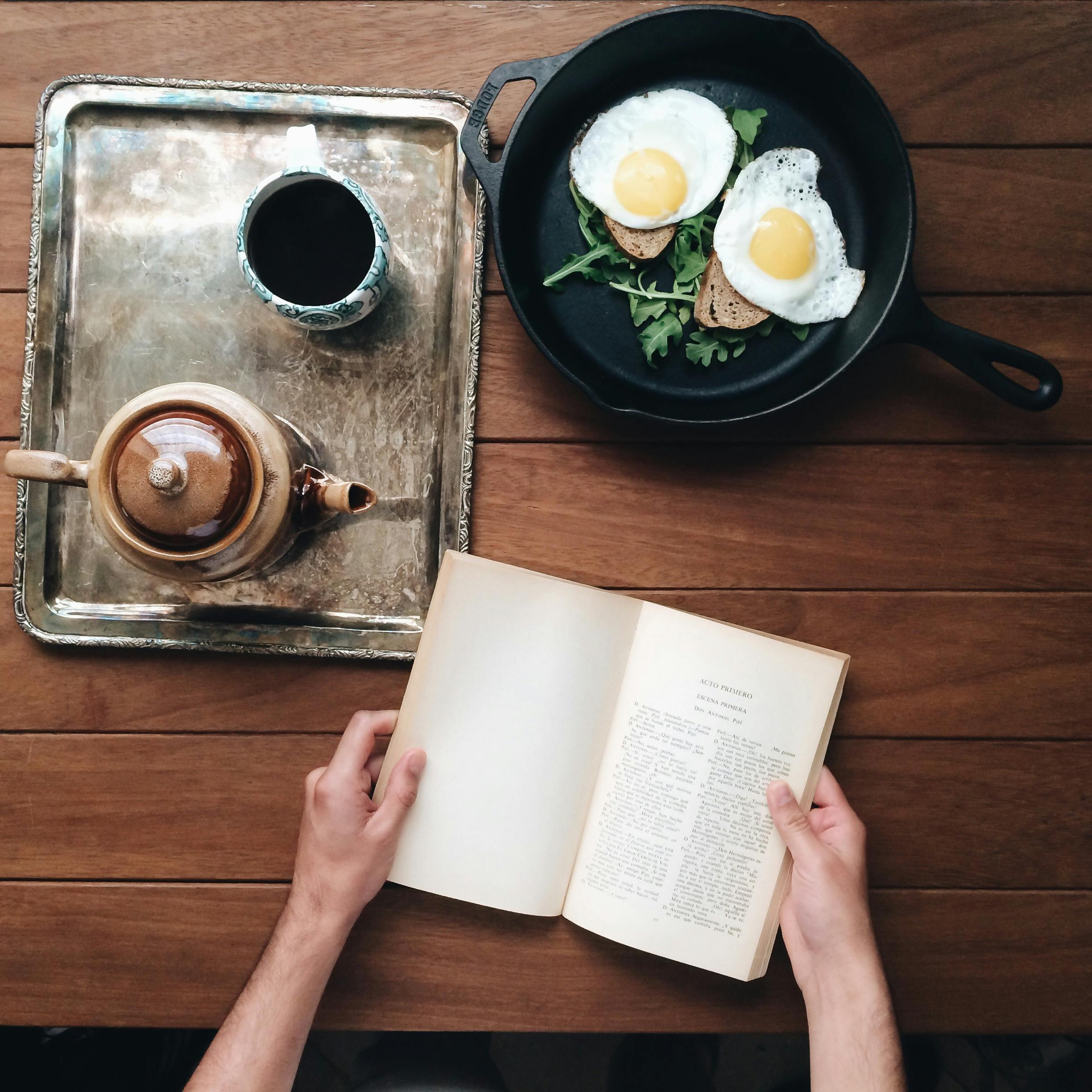 Crop person at table with book and breakfast